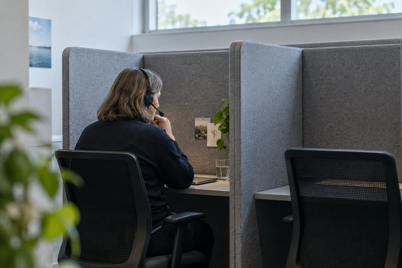 A helpline volunteer wearing a headset listens in a small booth lined with sound-absorbing panels, the booth beside her empty