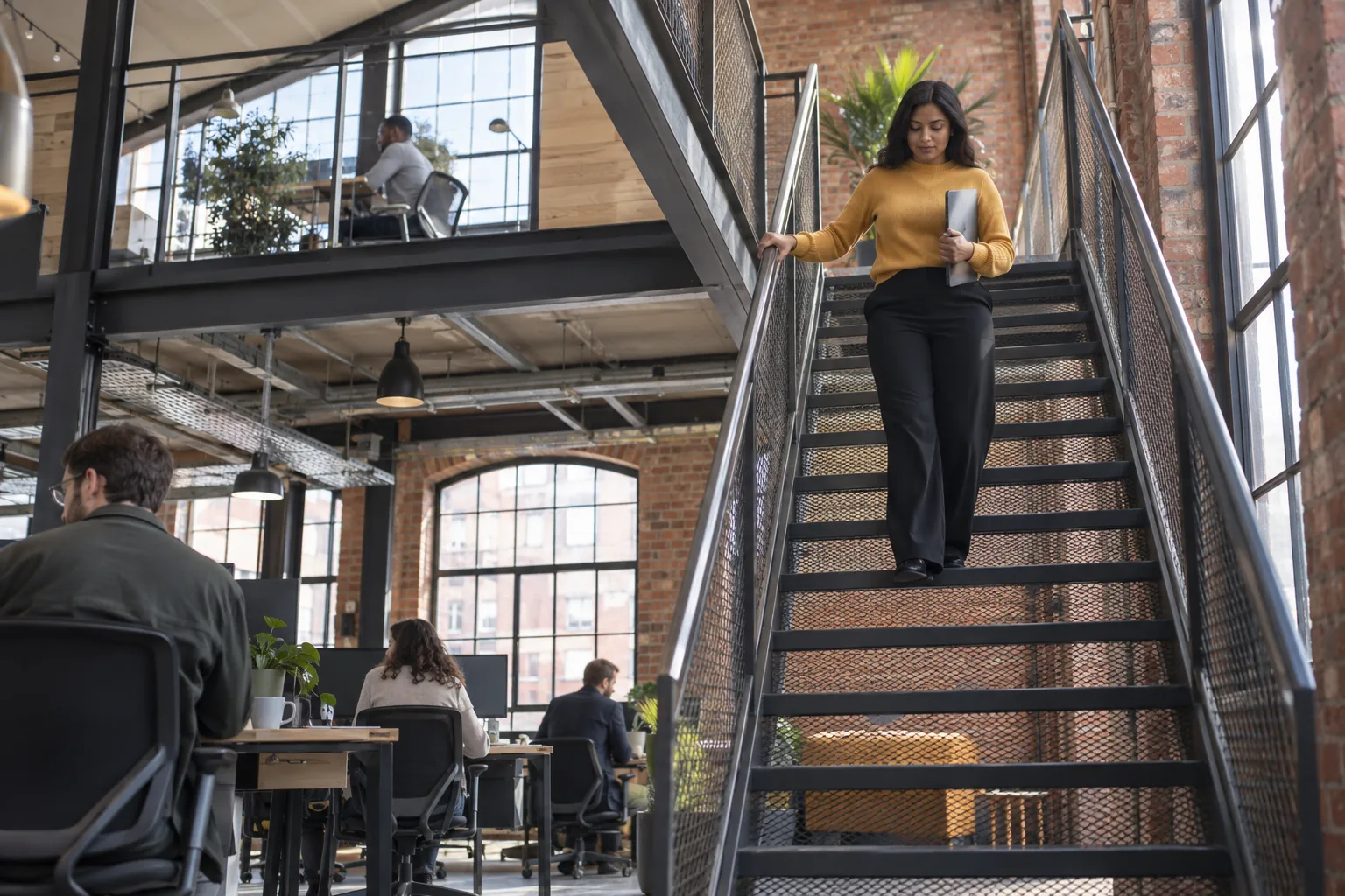 In a charity’s converted-warehouse head office, a compliance officer walks down an open steel staircase carrying a closed laptop, colleagues at desks on the floor below