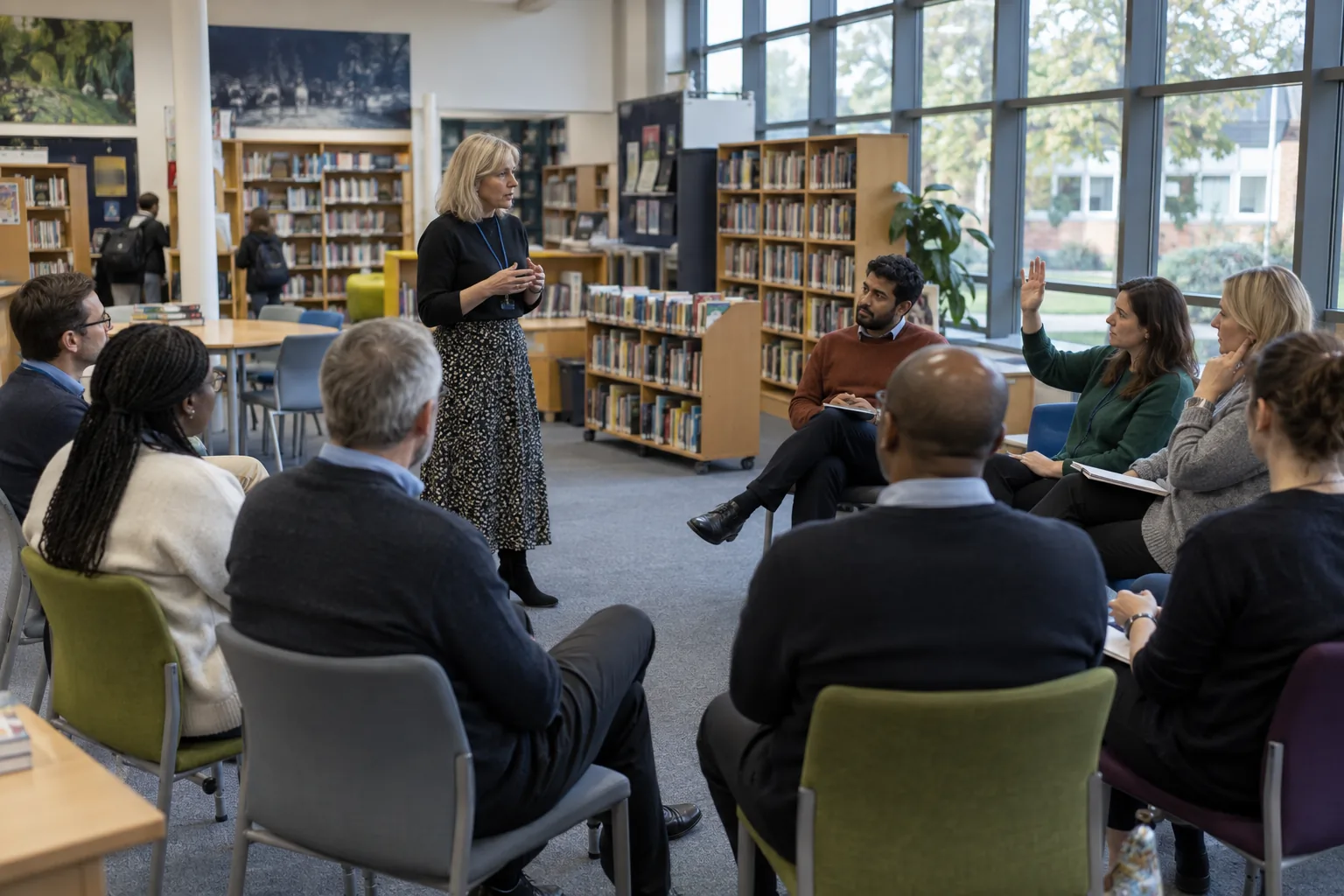 A designated safeguarding lead leads an after-school training session in a secondary school library, a dozen staff seated in a loose semicircle, one teacher asking a question